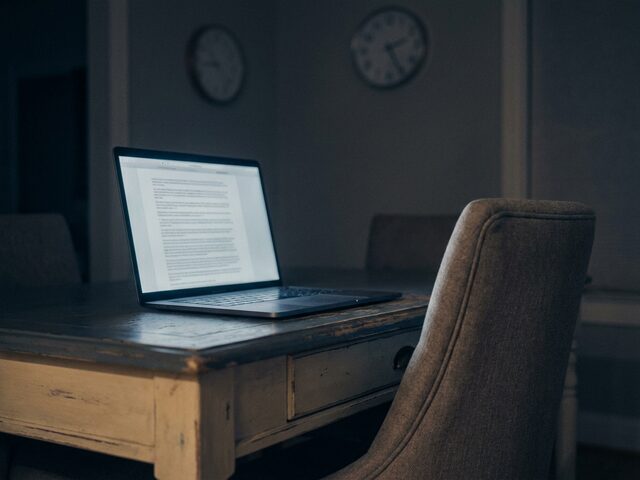 A laptop left open on an empty desk at night, screen still glowing.